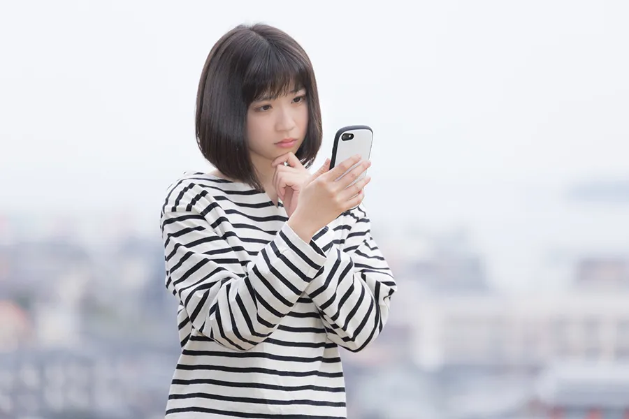 スマートフォンを眺めながら悩む女性